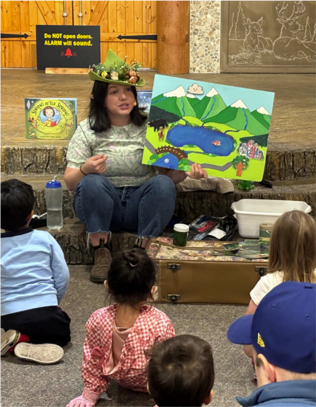 An educator holds an illustrated watershed scene during an interactive story time as children sit and listen.